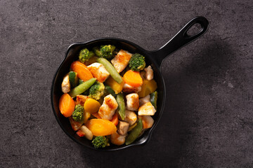 Stir fry chicken with vegetables on iron pan on black background. 	