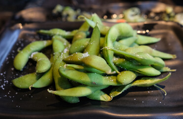 focus on salt-boiled edamame  serve on a black plate with blurred background