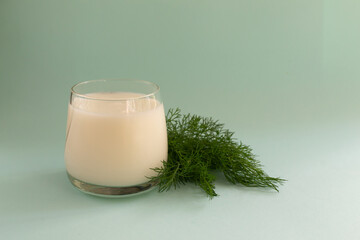 Obraz na płótnie Canvas Ayran in a glass glass with a sprig of dill on a blue background. Fermented product concept. Copy space.