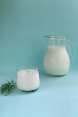 Ayran in a glass glass with a sprig of dill and a jug on a blue background. Fermented product concept. Copy space. Vertical orientation.