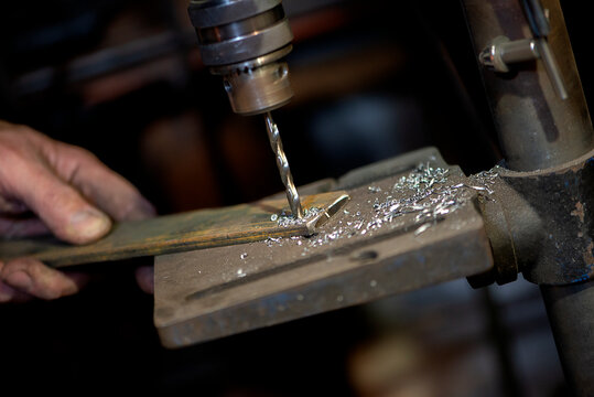 Blacksmith uses drill press in garage. A close up view of a metalworker operating a bench drill inside his workshop. Heavy duty machine is used for drilling a hole through metal. - Powered by Adobe