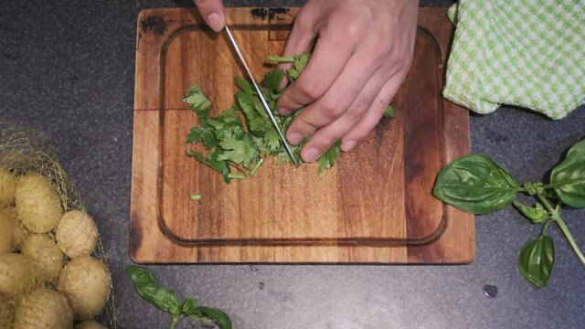Young male cutting celery in his kitchen on top of a cutting board with a sharp knife