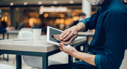 man in protective mask wiping the screen of a digital tablet with antiseptic