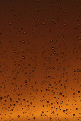 Rain drops on the window. Drops of water on glass, yellow and orange sunset in background.