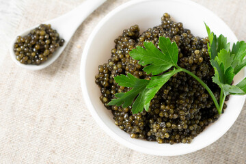 Black caviar. Black sturgeon caviar in a ceramic bowl and in a ceramic spoon on a light background. Useful delicacy. Top view with space for text	