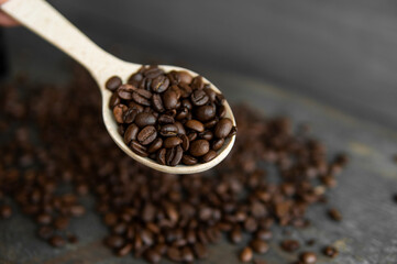 Fresh roasted arabica coffee beans in a wooden spoon and scattered coffee beans on a wooden table.