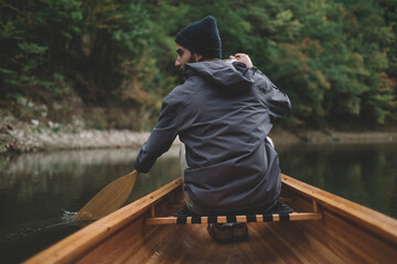 Autumn boat ride. Rear view of man paddling canoe on the forest lake