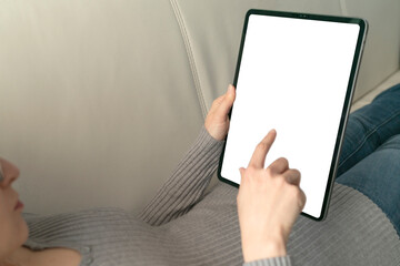 Template mockup tablet with white screen. A young woman use the tablet pc for socialize and shopping online on the sofa at home.