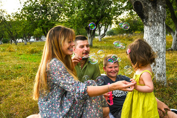 Parents blowing soap bubbles to child. Family love first. Family activity leisure outdoor in autumn park. Mother, father and two kids blow bubbles together