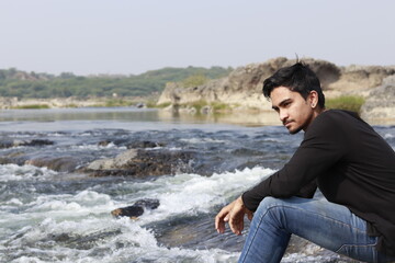 Young indian man sitting on the edge of river site