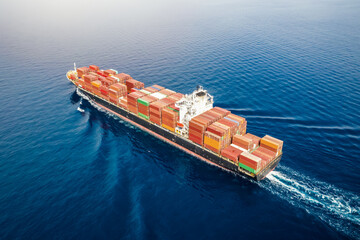Aerial view of a big, heavy loaded container cargo ship traveling with speed over blue sea