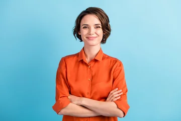 Fotobehang Photo of attractive charming lady cute bobbed hairdo arms crossed self-confident person worker friendly smile good mood wear orange office shirt isolated blue color background © deagreez