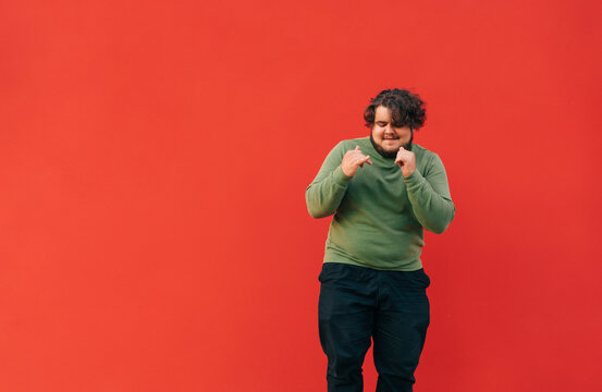 Positive overweight man and green sweatshirt funny dancing on red wall background and smiling. Fat man shows a dance performance. Isolated.
