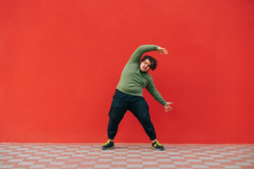Funny fat man in casual clothes trains on a red wall, looks at the camera and makes hand movements....
