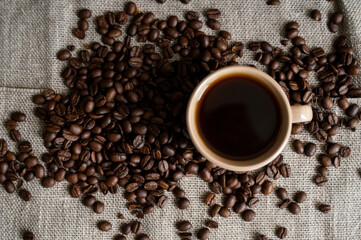 Coffee cup with roasted coffee beans on linen background. Mug of black coffe with scattered coffee beans. Fresh coffee beans.
