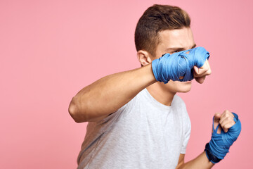 Guy in blue gloves on a pink background are boxing in a white t-shirt cropped view