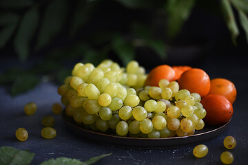 Summer still life with persimmons and grapes on a dark background