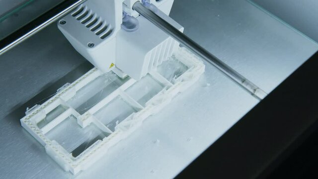 Camera Pans over a 3D Printer printing a Plastic Building model in an Architecture Firm