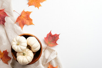 Autumn flat lay composition. Beige fabric, colorful maple leaves and bowl with pumpkins on white background. Top view. Autumn fall, harvest, thanksgiving concept.
