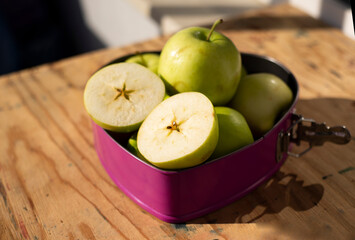  Green apples, whole and halved in a baking dish on a wooden table top.