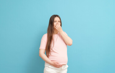 young pregnant woman in pink t-shirt on blue background, toxicosis during pregnancy