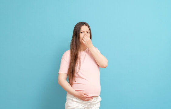 young pregnant woman in pink t-shirt on blue background, toxicosis during pregnancy