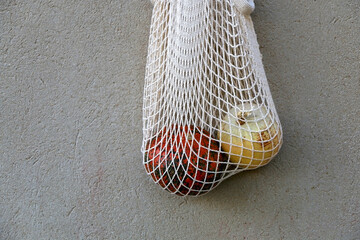 Two pumpkins in a mesh bag, hanging on a concrete wall.