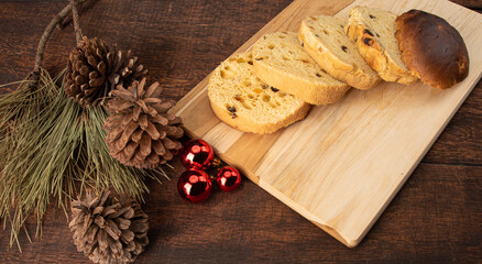 Panettone cut horizontally on a polished wood, pine cones and Christmas balls on rustic wood, black background, selective focus.