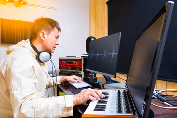 asian male music producer arranging a hit song on midi keyboard and computer. music production concept