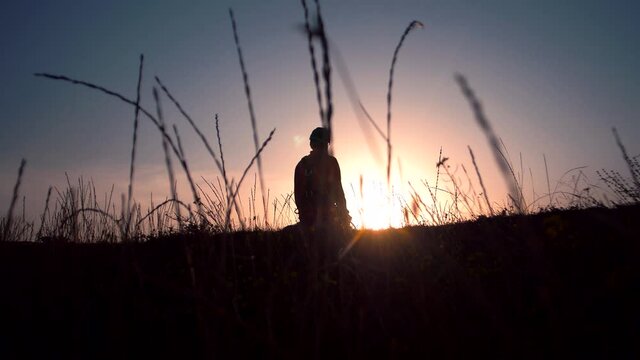 Silhouette of a man falls to his knees in a field against a sunset background