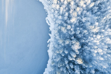 Аerial view of snow covered forest around beautiful lake. Rime ice and hoar frost covering trees....