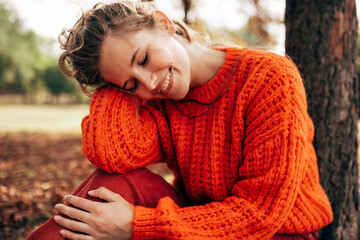 Outdoor image of a attractive young woman smiling, wearing orange knitted sweater posing on fall...
