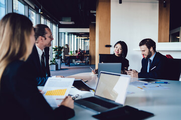 Prosperous team of finance experts in elegant formal wear discussing business planning enjoying productive cooperation, group of confident woman and man employees creating startup together