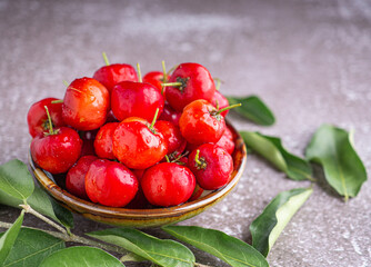 Ripe red cherries in a ceramic bowl with leaves on stone background. Space for text. Sweet organic berries. Concept of healthy fruits