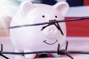 Pink piggy bank and barbed wire against United States national flag as symbol of economic war, sanctions and embargo busting.