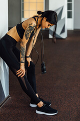 Fototapeta na wymiar Sportswoman leaning a wall in gym resting during training with skipping rope