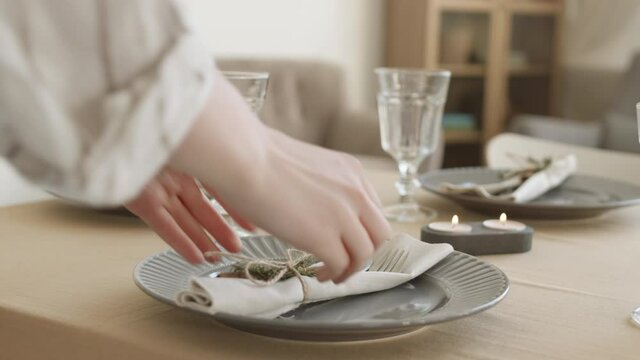 Close up of unrecognizable woman putting cutlery wrapped in beautiful napkin on plate standing on dining table