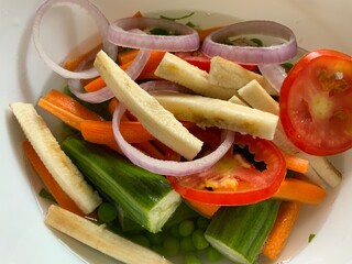 Dry cut vegetables like raw plantain onion rings tomatoes carrots and moringa placed on a white bowl in an isolated background © Tharun