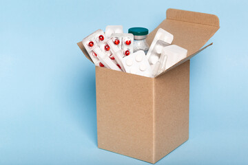 Delivery of medicines home from the pharmacy. Cardboard box with medicines, pills, bottles, injections isolated on blue background.