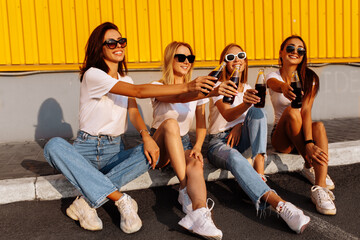 Obraz premium Young happy friends drink a drink and have fun together on a sunny summer day against the background of a yellow wall, the concept of friendship and celebration.