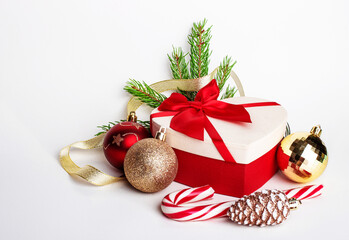 On a white background lies a gift with a red bow, Christmas balls, green spruce branches and a lollipop cane. Christmas decor. Christmas concept