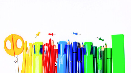 Bright yellow, red, blue and green markers, pencils and pens, a ruler and scissors lie on a light background. Copy space.