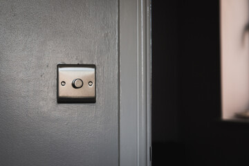 Moody image of a light switch mounted on a freshly painted wall. Chrome, fancy expensive and posh house decor on a new build with a fader switch mode on the panel in a dark house. Interior design.