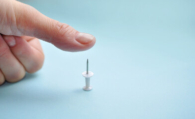 Thumb over push pin on blue background with copy space