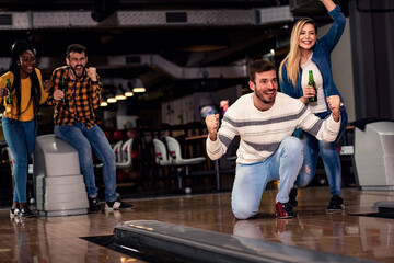 Group of friends enjoying time together laughing and cheering while bowling at club.