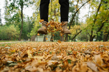 Happy man in boots jumping on yellow fallen leaves in the park. Autumn Park. Happy autumn