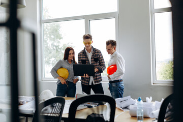 A team of professional young architects work in an office, one of them holding a laptop