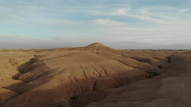 Drone flies over sandstone desert towards one hill and Mountain in the background.