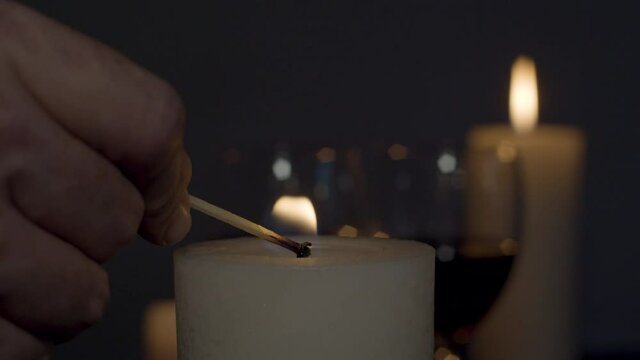 Candle being lit with match with a glass of wine and burning candle on background