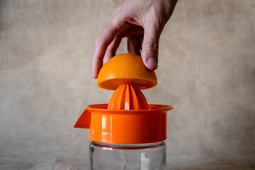 Hand squeezing orange in manual juicer. Soft beige background.